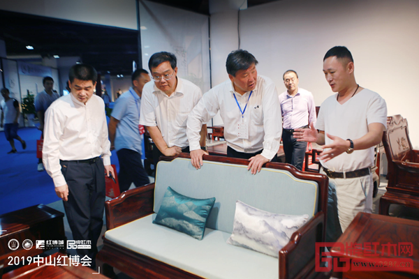 古木印象董事长周洪根（右一）向前来参观的领导、专家介绍古木印象产品的工艺及设计理念